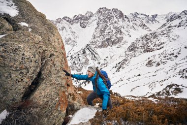 Turist dreadlocks ile karlı dağlar arka plan kayaya tırmanıyor