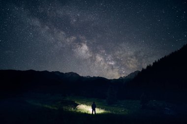 İnsanoğlunun silueti, gecenin karanlığında gökyüzünün altında yıldızlarla aydınlık bir alan aydınlatıyor..