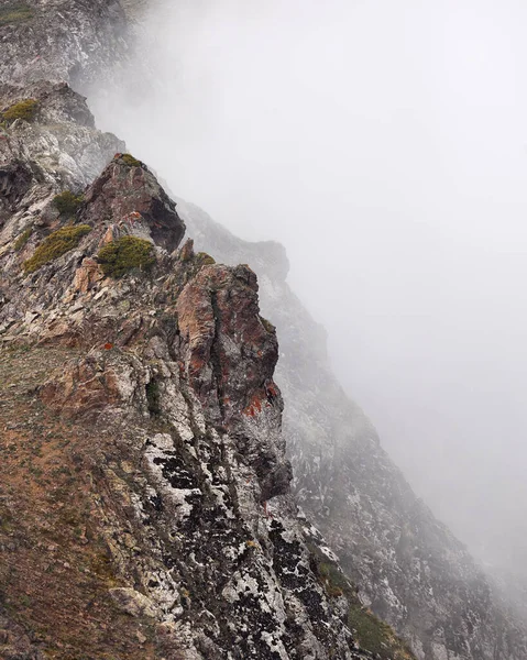 Landscape of snow mountain valley with rock in shape of the face against cloudy fogy sky in Kazakhstan