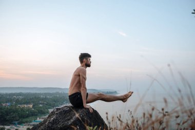 Sağlıklı adam gün batımında Yoga plaj altında uygulamak.