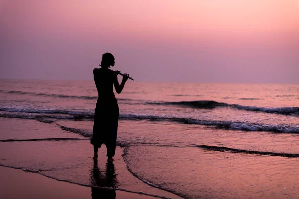 Un homme s'entraîne à jouer de la flûte sur la plage au coucher du soleil. GOA, Inde. 16.01.2018 — Photo