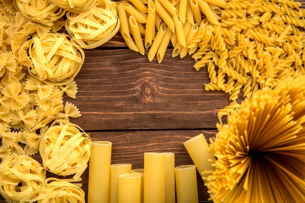 Tema da pasta. Diferentes tipos de macarrão em um fundo de madeira. Farfalle, fettuccine, macarrão, fusilli e penne rigate — Fotografia de Stock