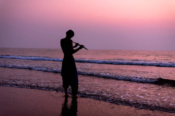 Un homme s'entraîne à jouer de la flûte sur le bouleau au coucher du soleil. GOA, Inde. 16.01.2018 — Photo