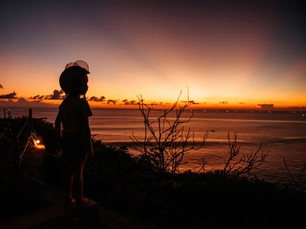 Un garçon dans un casque regarde le coucher du soleil en mer sur le point de vue — Photo