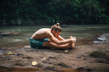 Yoga uygulaması ve doğada meditasyon. Nehir yakınlarında pratik yapan adam