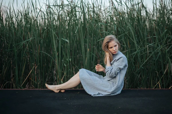 부두에 앉아 파란색 드레스에 로맨틱 한 소녀. 식물성 배경 — 스톡 사진