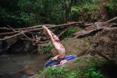 Yoga uygulaması ve doğada meditasyon. Nehir yakınlarında pratik yapan adam