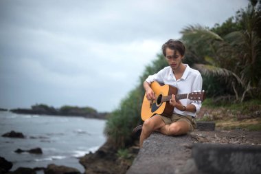 Sahilde gitar çalan romantik bir genç adam.