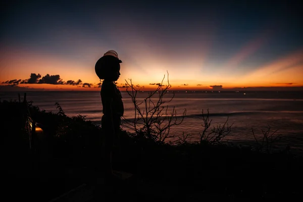 En pojke i en hjälm tittar på solnedgången till sjöss på utsiktsplatsen — Stockfoto
