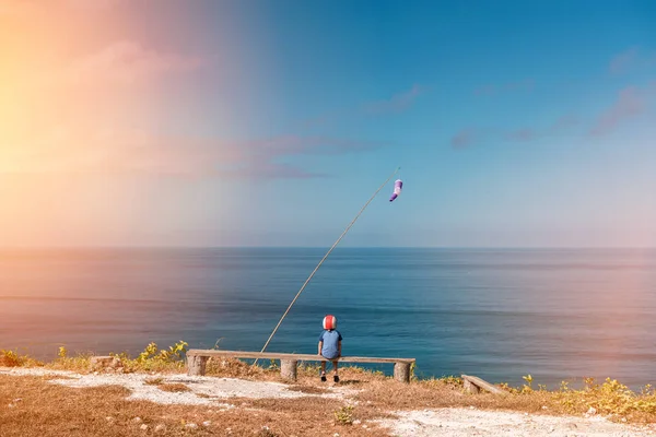 Dreaming boy sits on a bench in a helmet on the background of the sea. View point — Stock Photo, Image