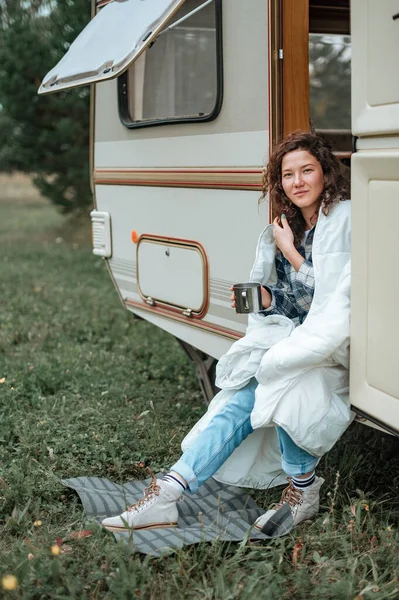 Fille assise sur l'échelle du camping-car avec une tasse dans les mains enveloppé dans une couverture — Photo