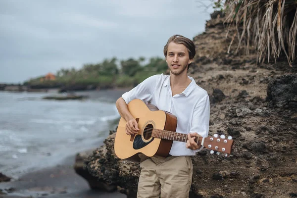 Sahilde gitar çalan romantik bir genç adam.