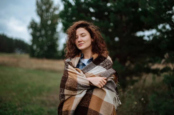 Aantrekkelijk meisje verpakt in een geruite ruit op een bos en veld achtergrond — Stockfoto