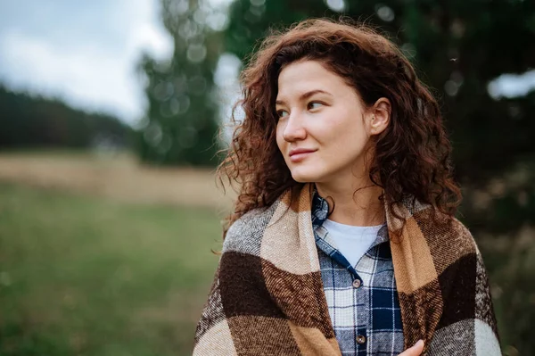 Aantrekkelijk meisje verpakt in een geruite ruit op een bos en veld achtergrond — Stockfoto