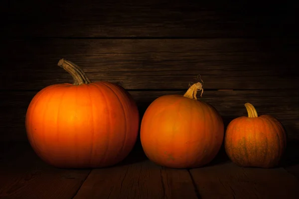 Drei herbstliche Halloween-Kürbisse auf dunklem Holzgrund — Stockfoto