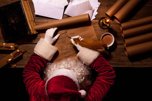 Weihnachtsmann sitzt am Tisch in seinem Zimmer und schreibt Weihnachtsbriefe oder Wunschzettel — Stockfoto