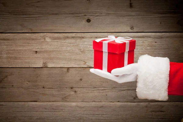圣诞老人手拿着一个红色礼品盒在木背景 — 图库照片