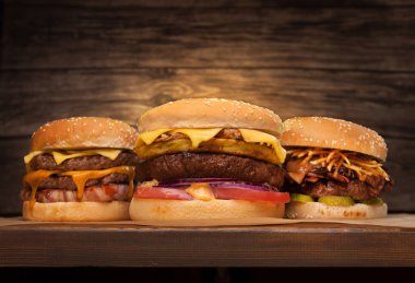 Ahşap zemin üzerinde üç büyük hamburger. Düşük açılı ön görünüm. Metniniz için kopya alanı.