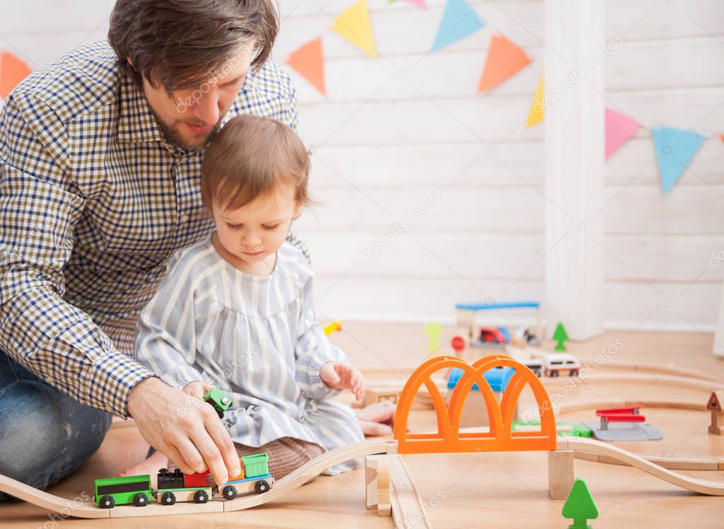 Cute baby girl and her father playing with toy railway road