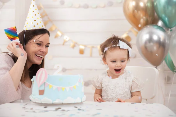 Fiesta de cumpleaños del bebé. Madre y su hija celebran y se divierten juntas. Fiesta infantil con decoración de globos y tarta Imágenes De Stock Sin Royalties Gratis