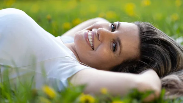Femme s'allonge sur l'herbe verte, se détendre à l'extérieur regardant heureux et souriant — Photo