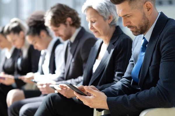 Grupo de empresários com smartphones sentados em uma fileira — Fotografia de Stock