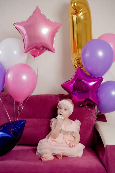 Birthday girl bites a piece of cake sitting on the sofa surrounded by balloons — Stock Photo, Image