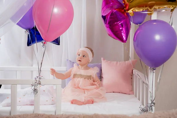 A criança brinca com o presente de um balão enquanto se senta na cama no seu primeiro aniversário — Fotografia de Stock