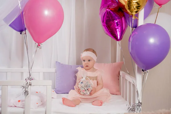 A criança brinca com o presente de um balão enquanto se senta na cama no seu primeiro aniversário — Fotografia de Stock