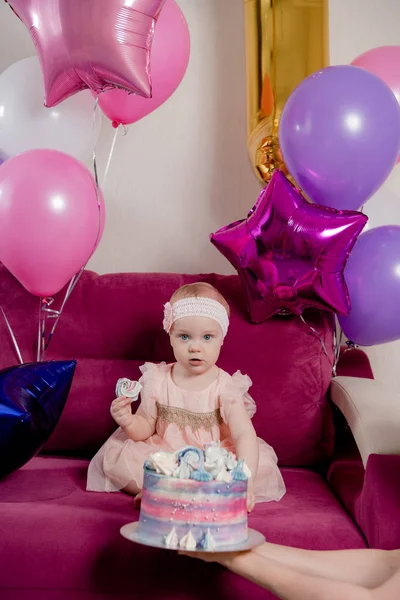 Birthday girl bites a piece of cake sitting on the sofa surrounded by balloons Stock Picture
