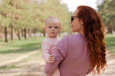 kız çocuk ormanda yürürken kollarını tutar. Bebek, Anne gülümser de ciddi bir göz ile kameraya benziyor. Pembe ve mor kıyafetlerle giyindin