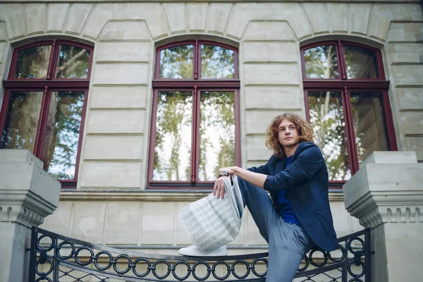 Young reddish man reading newspaper near old style building