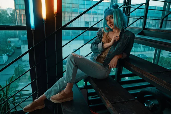 Stilvolle Frau mit blauer Perücke sitzt auf der Treppe in einem modernen — Stockfoto