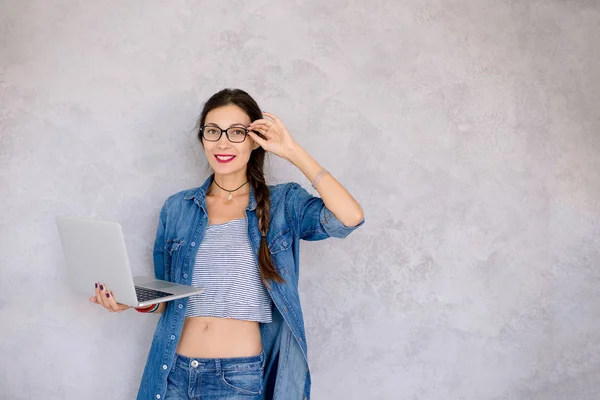 Mulher bonita em óculos de pé com um laptop em que ele — Fotografia de Stock