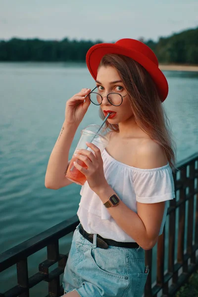 Молодая стильная женщина выпивает освежающий напиток во время ходьбы — стоковое фото