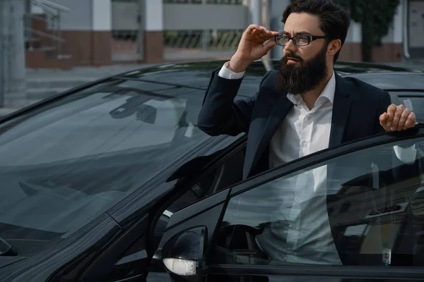 Confident man in formal wear holding hand on opened car door wat — Stock Photo, Image