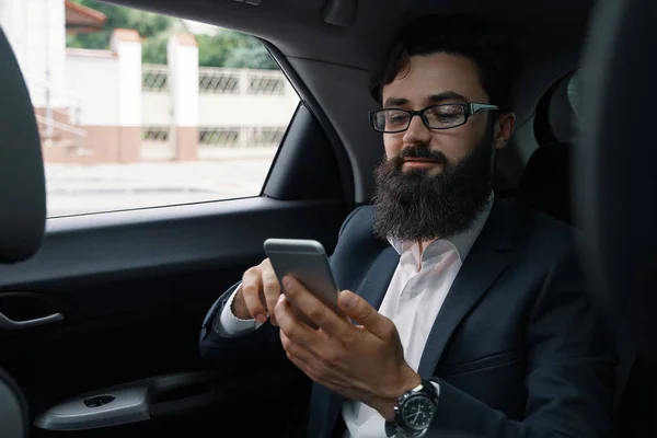 Um homem de negócios enquanto viaja de carro no banco de trás usando um sm — Fotografia de Stock