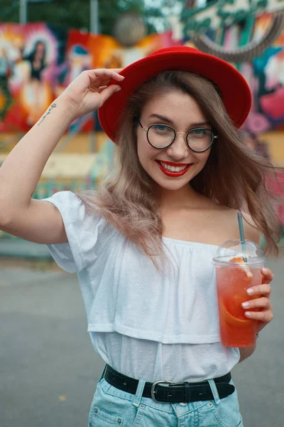 Cheerful young woman holding a drink while smiling — Stock Photo, Image