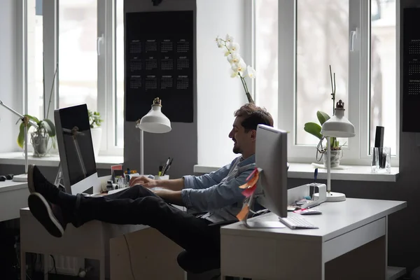 Giovane uomo barbuto intelligente che lavora e sorride al loft moderno — Foto Stock