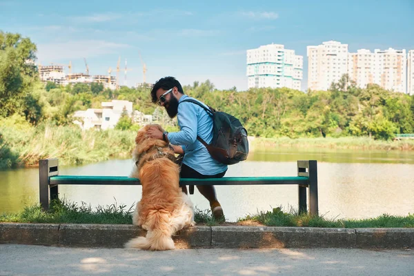 Молодой человек, сидящий со своей собакой на стуле в парке и обнимающий — стоковое фото
