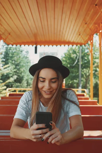 Молода дівчина-хіпстерка в модному капелюсі тримає смартфон в руках — стокове фото