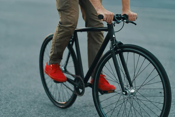 Closeup of casual man legs riding classic bike on city gray road wearing red sneakers and comfy pants. Copy space