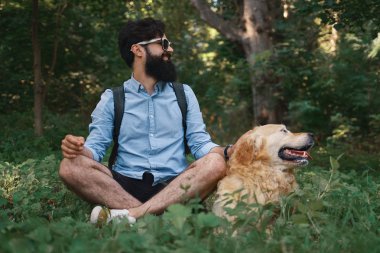 Yakışıklı adam çimlere oturup istirahat sevimli köpeği ile bacak bacak, gülümseyerek, hem sol, aynı yöne bakıyor, gün mükemmel. İnsan ve hayvan arasındaki dostluk. Mutlu arkadaş.