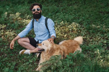 Yakışıklı adam çimlere oturup istirahat gülümseyen ve mükemmel bir gün zevk ile onun sevimli köpek, bacak bacak. İnsan ve hayvan arasındaki dostluk. Mutlu arkadaş.