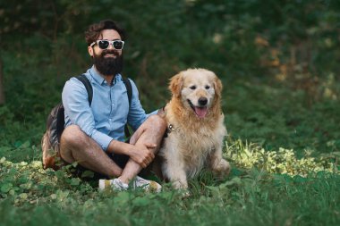 Yakışıklı adam çimlere oturup istirahat gülümseyen ve mükemmel bir gün zevk ile onun sevimli köpek, bacak bacak. İnsan ve hayvan arasındaki dostluk. Mutlu arkadaş.