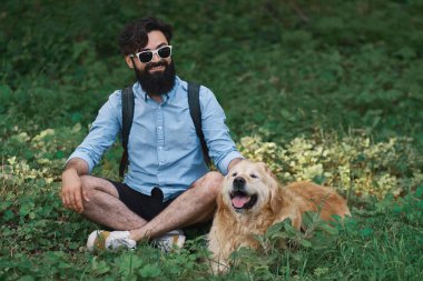 Yakışıklı adam çimlere oturup istirahat gülümseyen ve mükemmel bir gün zevk ile onun sevimli köpek, bacak bacak. İnsan ve hayvan arasındaki dostluk. Mutlu arkadaş.