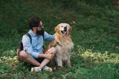 Yakışıklı adam çimlere oturup istirahat gülümseyen ve mükemmel bir gün zevk ile onun sevimli köpek, bacak bacak. İnsan ve hayvan arasındaki dostluk. Mutlu arkadaş.