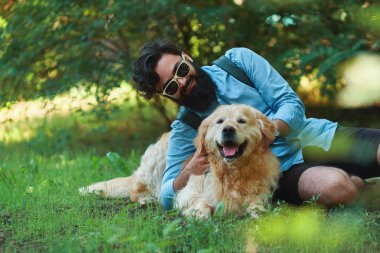 Sakal ve oynama ve güneşli bir gün, Doğa ve dostluk zevk küçük sarı köpeği olan adam. Gök mavisi bir gömlek ve güneş gözlüğü hayvanını taping sakallı adam.