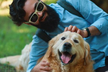 Sakal ve oynama ve güneşli bir gün, Doğa ve dostluk zevk küçük sarı köpeği olan adam. Gök mavisi bir gömlek ve güneş gözlüğü hayvanını taping sakallı adam.
