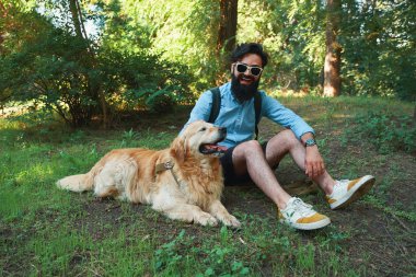 Sakal ve oynama ve güneşli bir gün, Doğa ve dostluk zevk küçük sarı köpeği olan adam. Gök mavisi bir gömlek ve güneş gözlüğü hayvanını taping sakallı adam.
